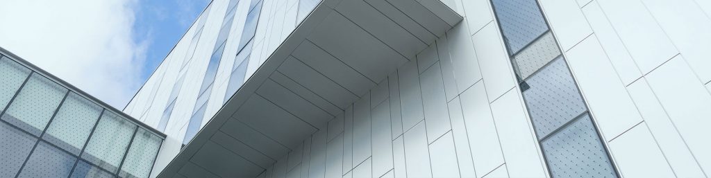 A modern office building with an overhanging upper story. It makes interesting geometric shapes against a sunny sky.